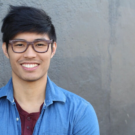Smiling person wearing glasses and denim shirt.